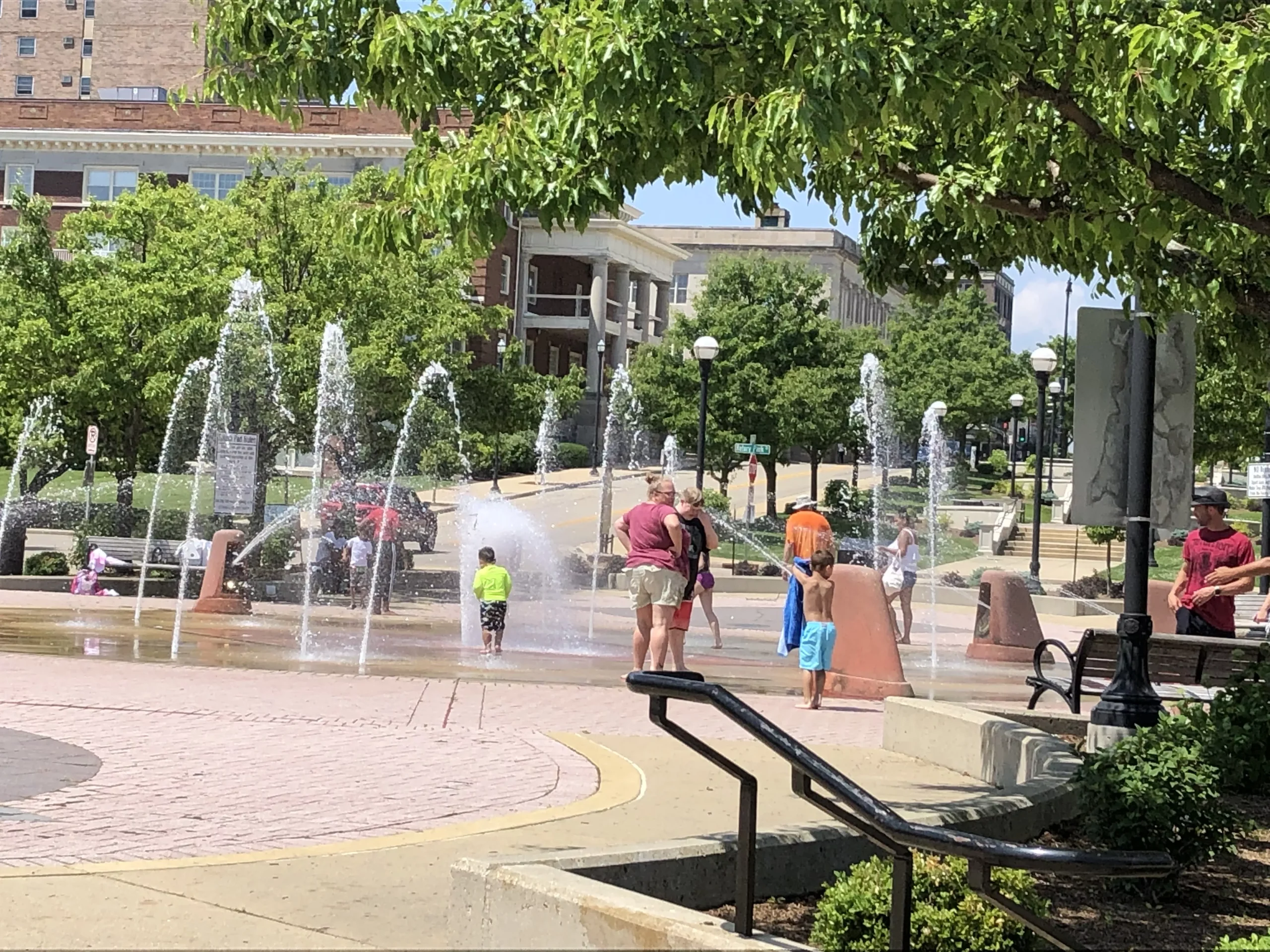 Children and adults playing in a public splash fountain on a sunny day in Racine.