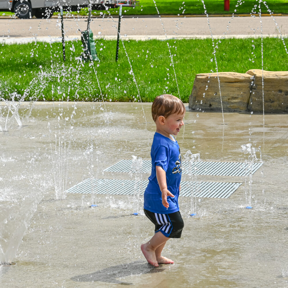 Child playing in sprinkler-style water at Point to Point Park splash pad.
